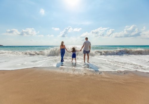 Family holding child's hands on sunny beach